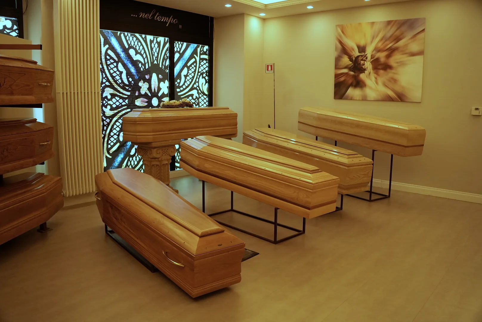 Sala esposizione con cofani in legno chiaro davanti a una vetrata artistica